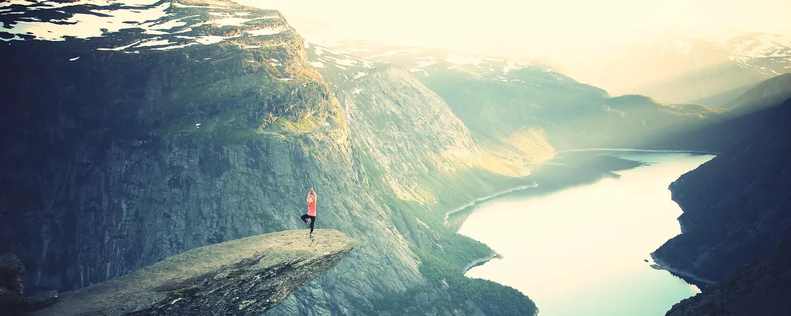 A person standing on a cliff above a fjord