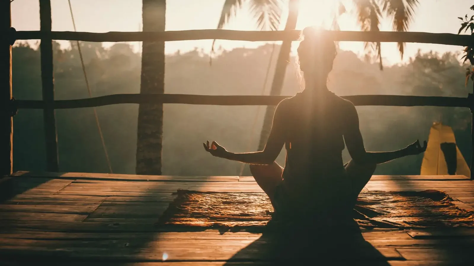 A woman meditating on a wooden deck at sunrise