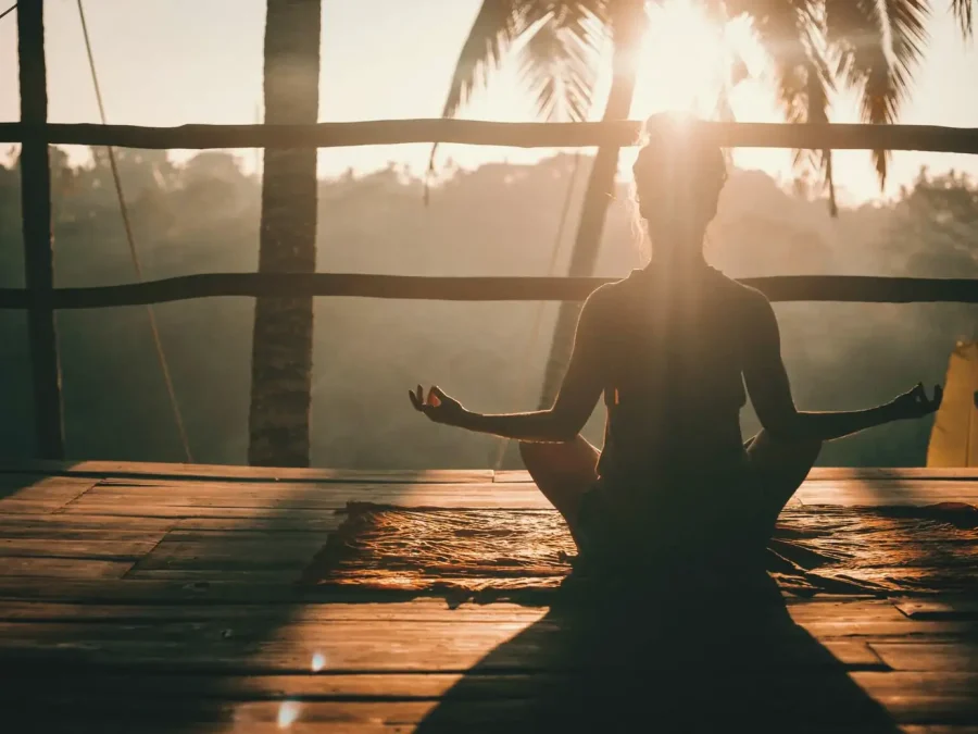 A woman meditating on a wooden deck at sunrise