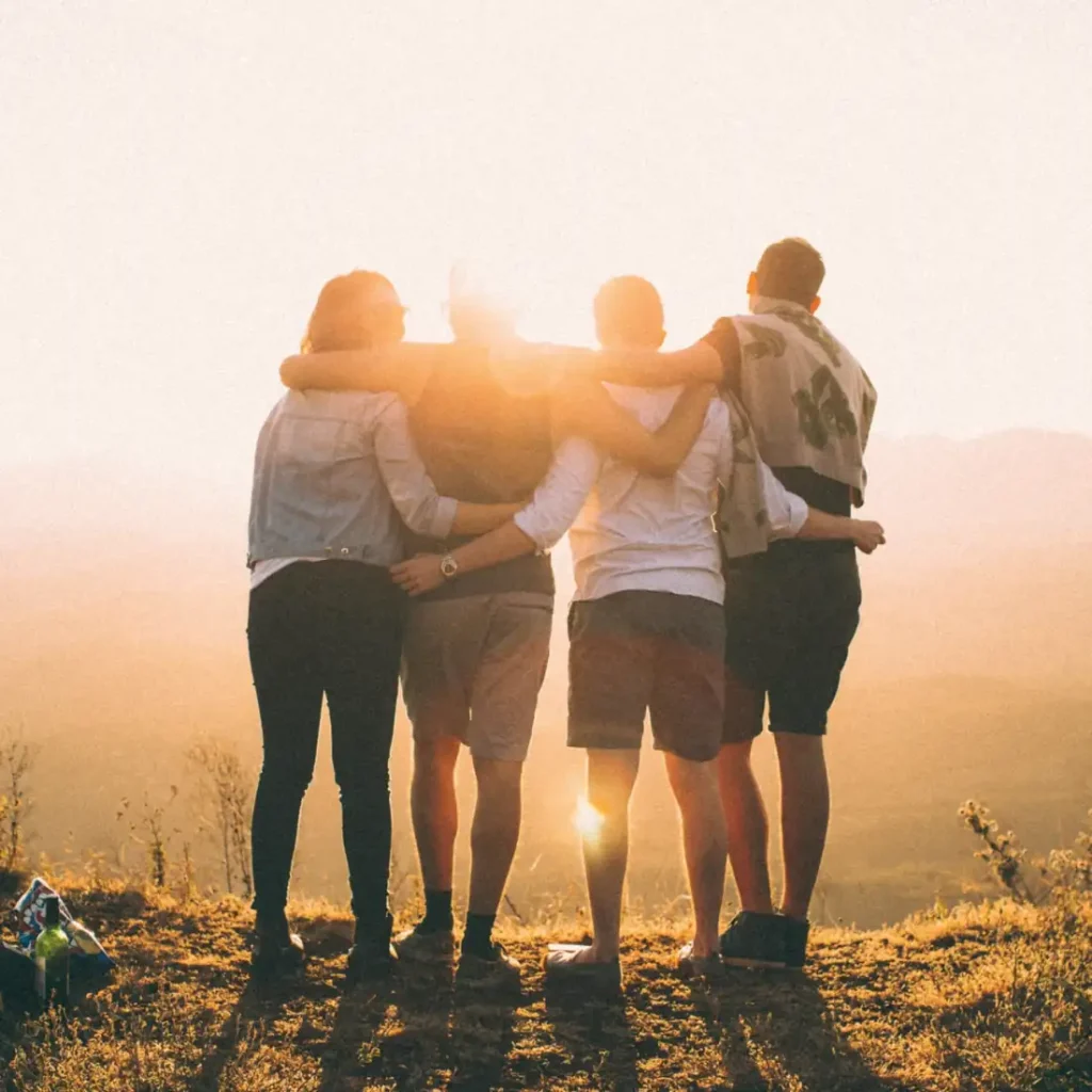 Four friends with arms around each other at sunset