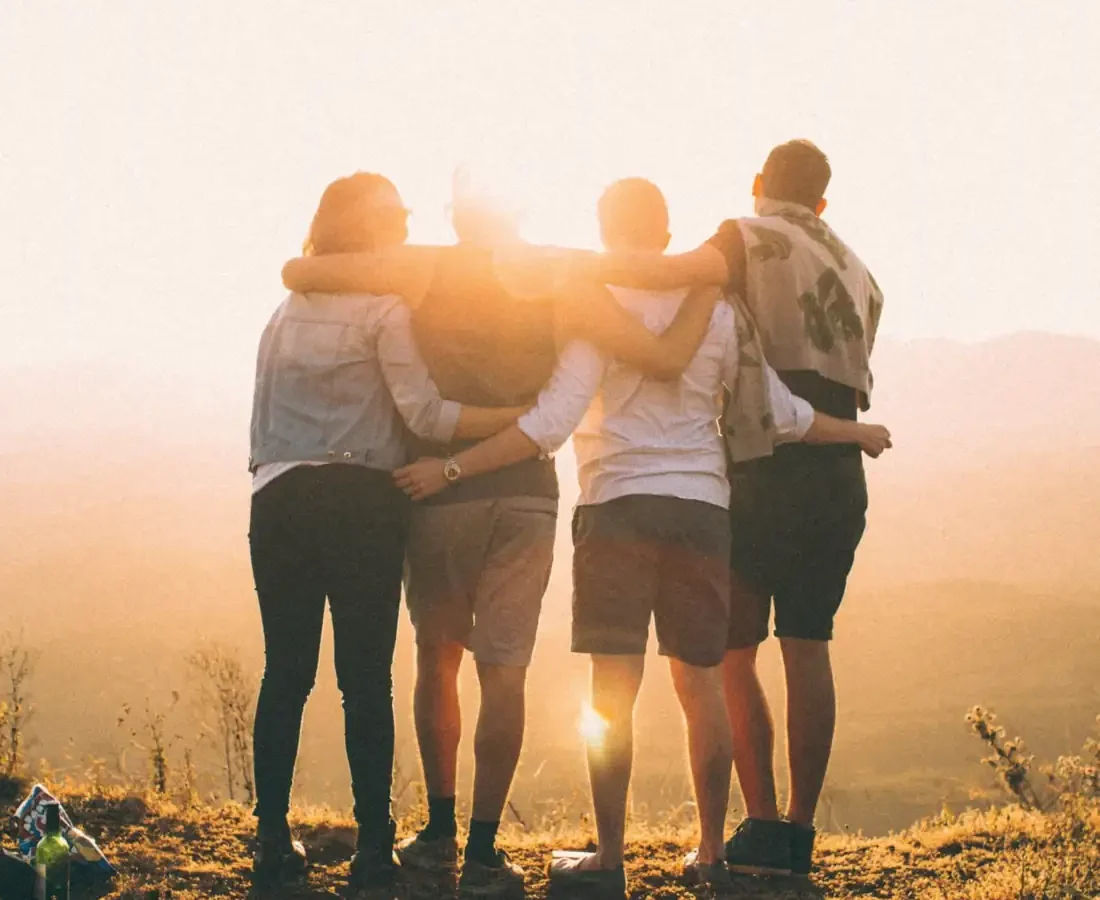 Four friends with arms around each other at sunset