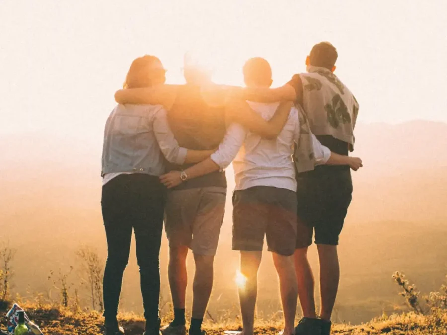 Four friends with arms around each other at sunset