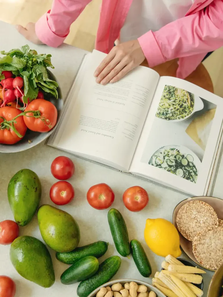 Fresh vegetables, fruit and an open cookbook on a table