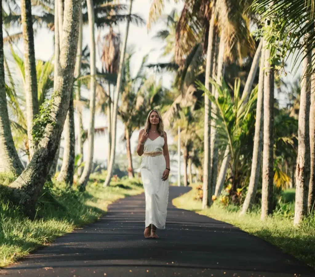 A woman in white walking down a road lined with palm trees
