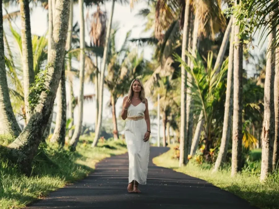 A woman in white walking down a road lined with palm trees