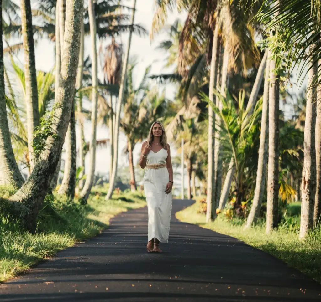 A woman in white walking down a road lined with palm trees
