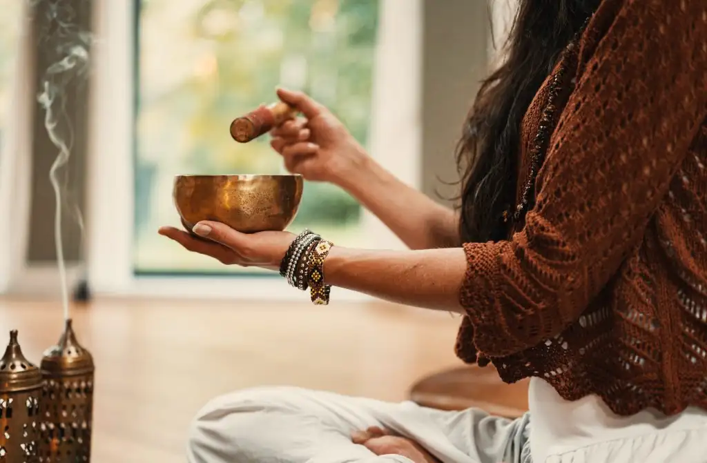 Hands playing a brass singing bowl beside incense