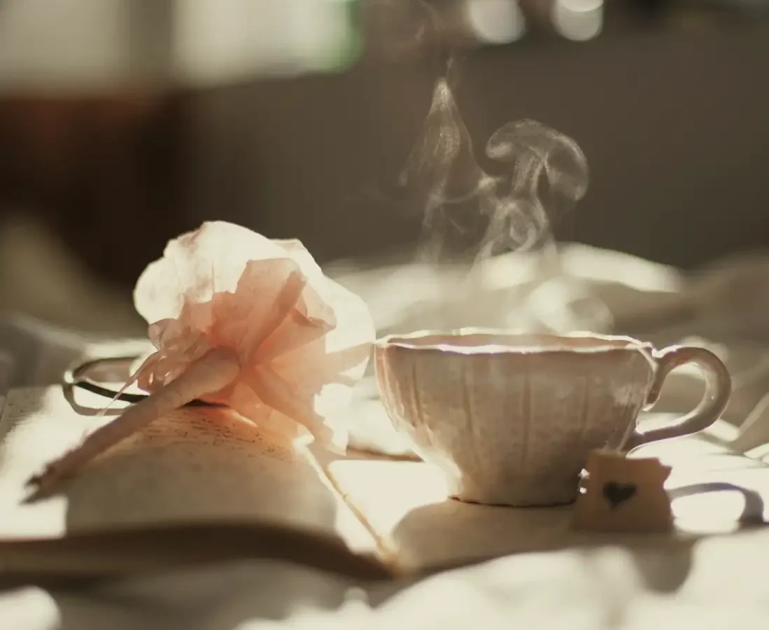 A steaming cup of tea beside an open book